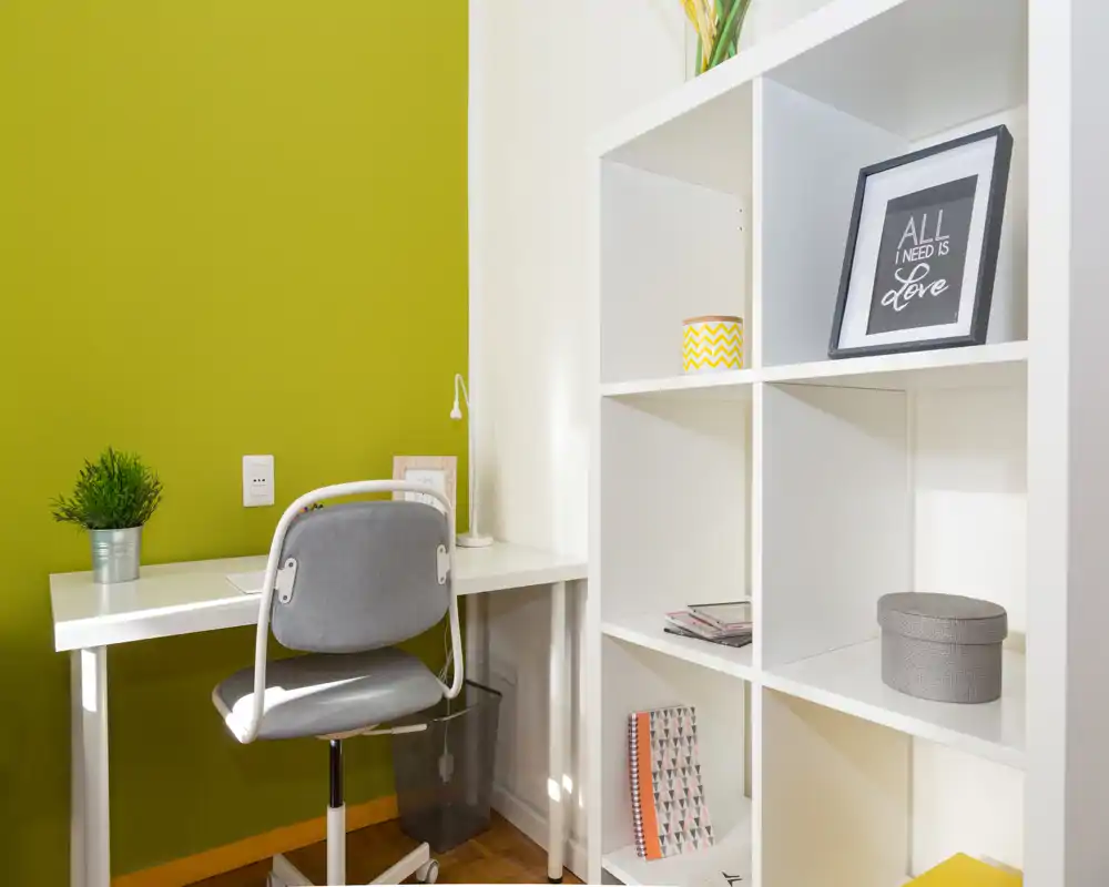 Compact workspace corner with a white desk, grey chair and open shelving; bright, modern styling with a green accent wall and neat decorative details.