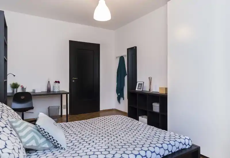 Bright, modern bedroom with patterned bedding, a workspace desk and shelving—clean minimalist styling and good natural light.