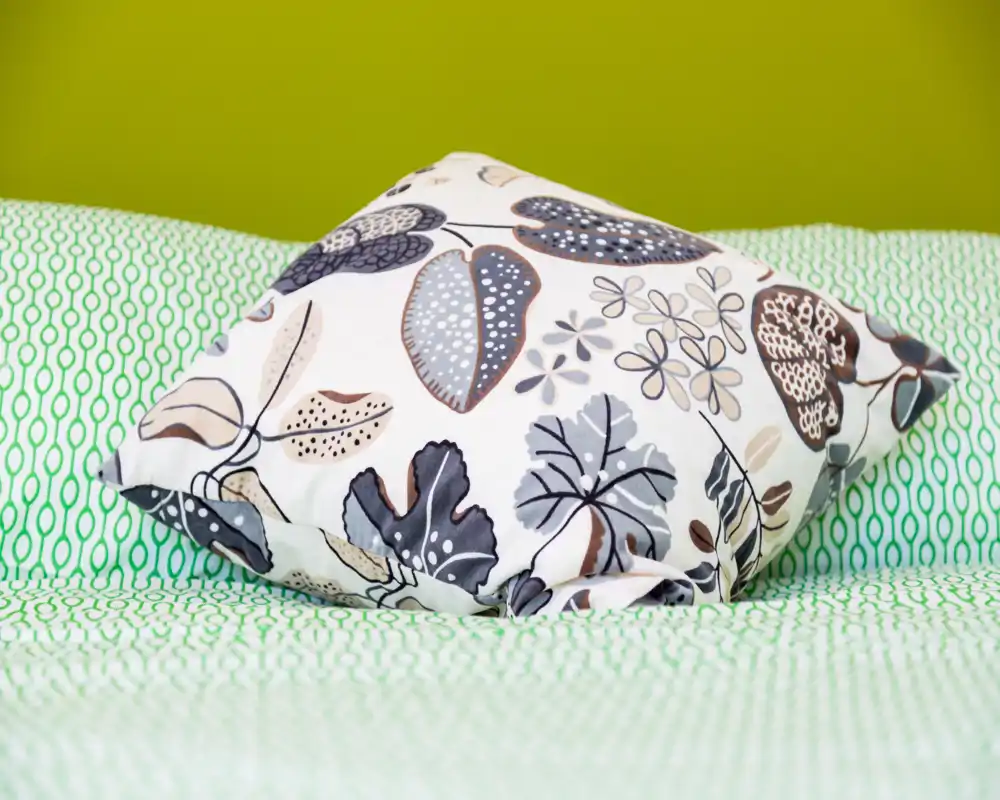 Primo piano di un cuscino decorativo e della biancheria da letto davanti a una parete verde brillante — immagine nitida e colorata che mette in risalto i tessuti e i motivi.