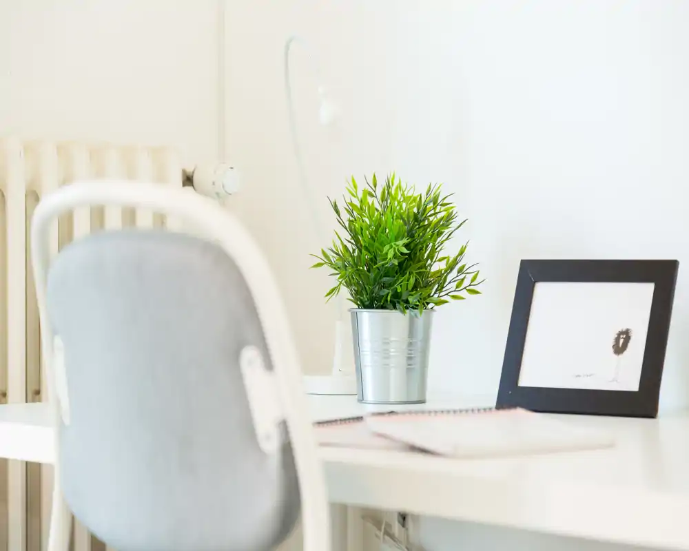 Angolo di lavoro luminoso e minimale con sedia, lampada da scrivania, pianta in vaso e cornice: un'area giorno/studio pulita e ariosa.