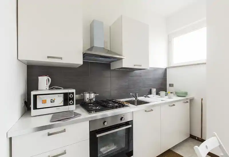 Cocina moderna y luminosa con muebles blancos, placa de gas, horno integrado y fregadero de acero; compacta y bien organizada para alquileres de corta estancia.