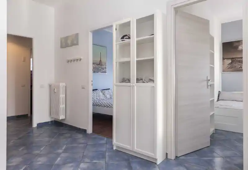 Bright, well-lit entrance/hallway with blue tiled floor, radiator and storage; two bedrooms visible through open doors, offering a clear view of apartment layout.