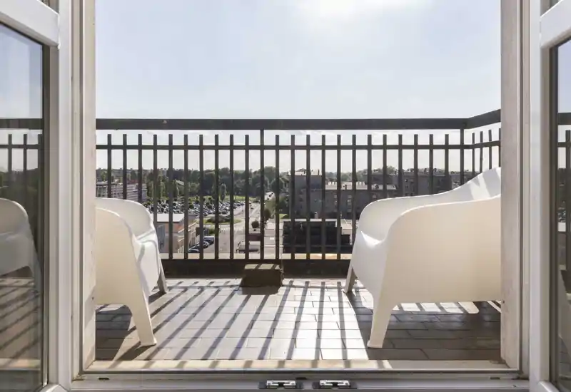 Sunny balcony with two modern white chairs and a metal railing, offering a clear city view — ideal for morning coffee.
