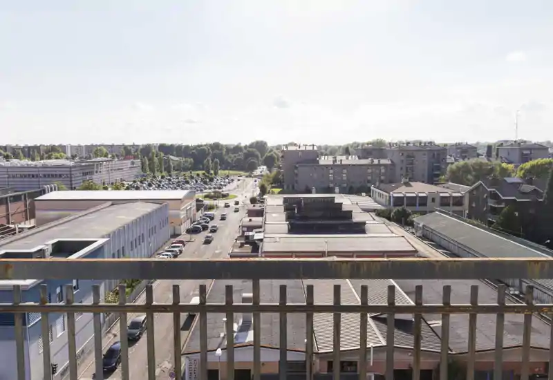 View from a balcony overlooking an urban street and low-rise buildings with good daylight—ideal to showcase outdoor space and city surroundings.