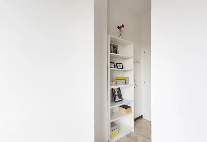 Ingresso ordinato con una sottile libreria bianca per scarpe e accessori; arredi neutri e buona luce naturale creano una prima impressione pulita e accogliente.