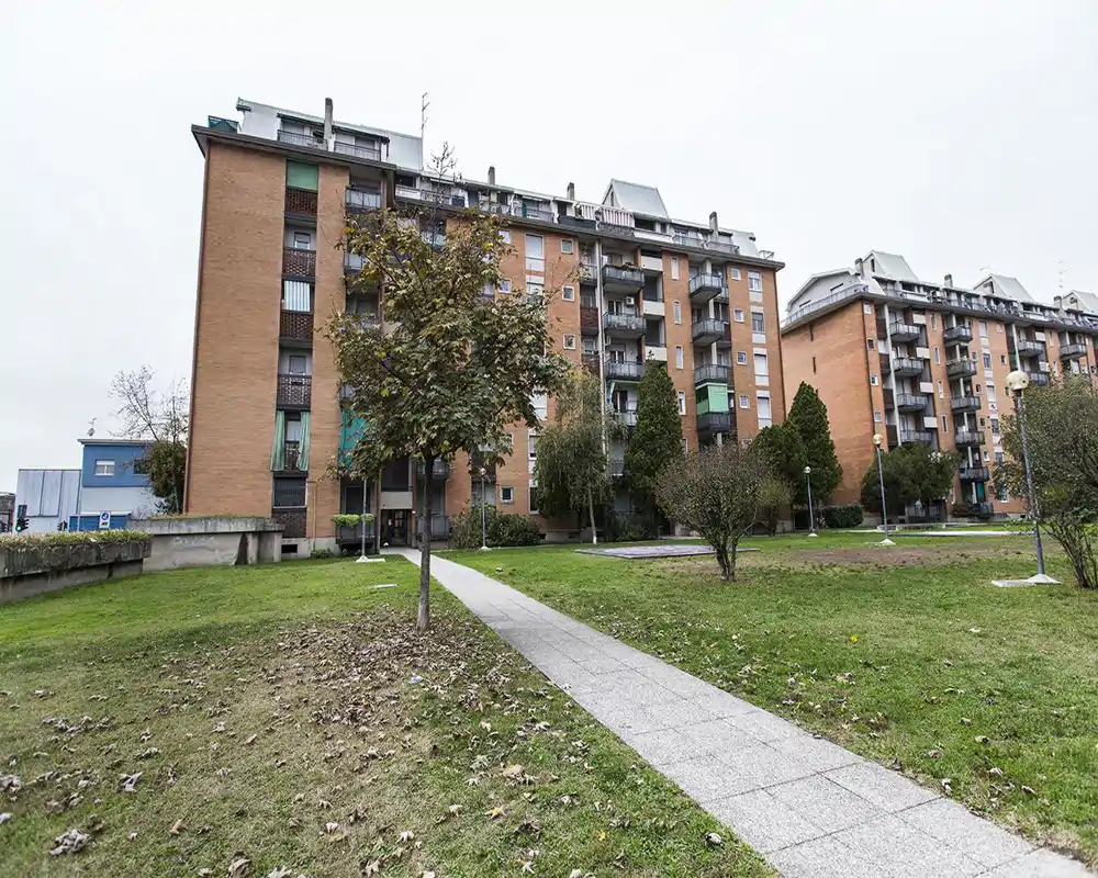 Spazio verde condominiale davanti ai palazzi con un percorso pedonale, alberelli e prati — ideale per momenti di relax.