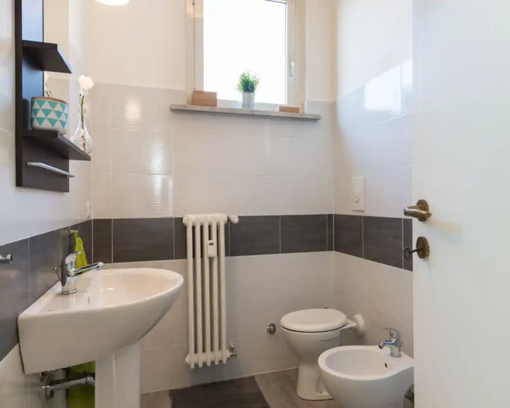 Bagno pulito e luminoso con lavabo, WC e bidet, piastrelle moderne e una piccola finestra che illumina naturalmente.