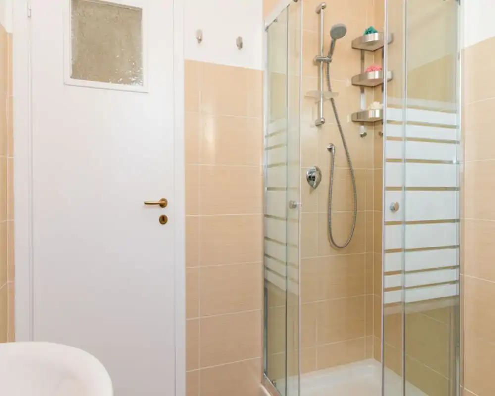 Bagno moderno e pulito con doccia a vetro, rubinetteria cromata e piastrelle color beige chiaro, ambiente luminoso e ordinato.