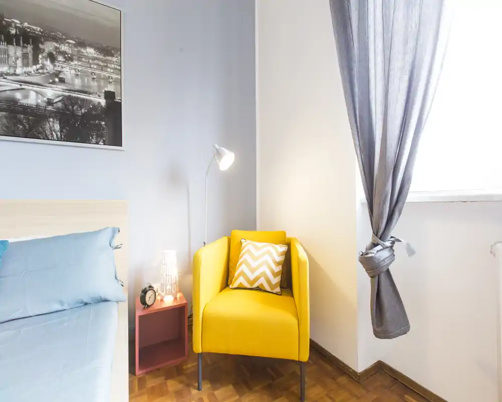 Bright, stylish bedroom corner with a visible bed, a cheerful yellow armchair, bedside table and lamp — an inviting spot for reading or relaxing.