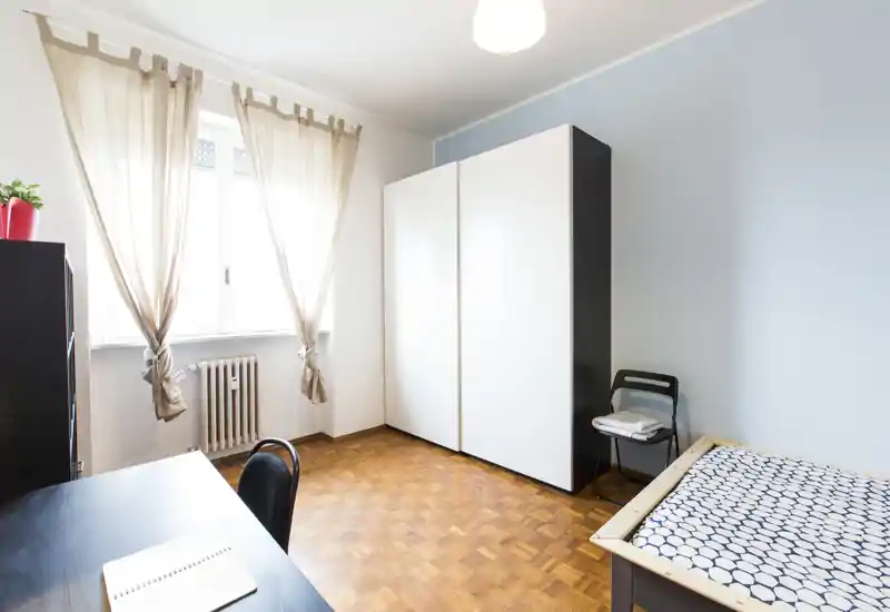 Dormitorio luminoso y sencillo con cama individual, gran armario y escritorio junto a la ventana; suelo de parquet limpio y decoración neutra que aporta tranquilidad.