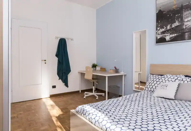 Bright, tidy bedroom with a patterned duvet, light-wood headboard and a small desk by the wall — ideal for a comfortable stay and work-from-room setup.