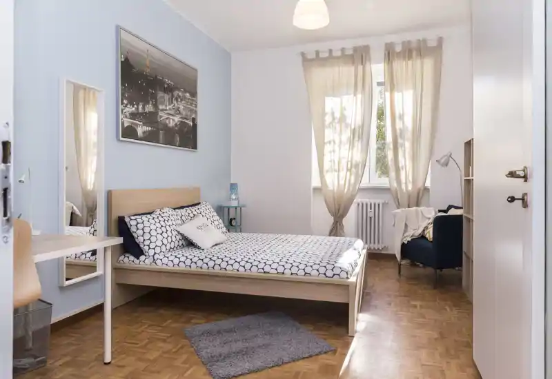 Bright, well-styled bedroom with a double bed, patterned bedding, soft curtains and a cozy reading chair by the window.