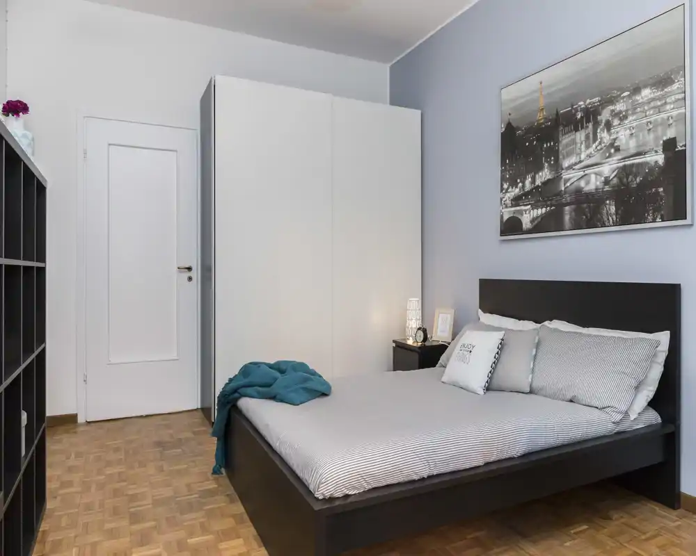 Camera da letto moderna e luminosa con letto matrimoniale, comodino e grande armadio bianco. Toni neutri e arredo minimale creano un'atmosfera calma e accogliente ideale per affitti brevi.