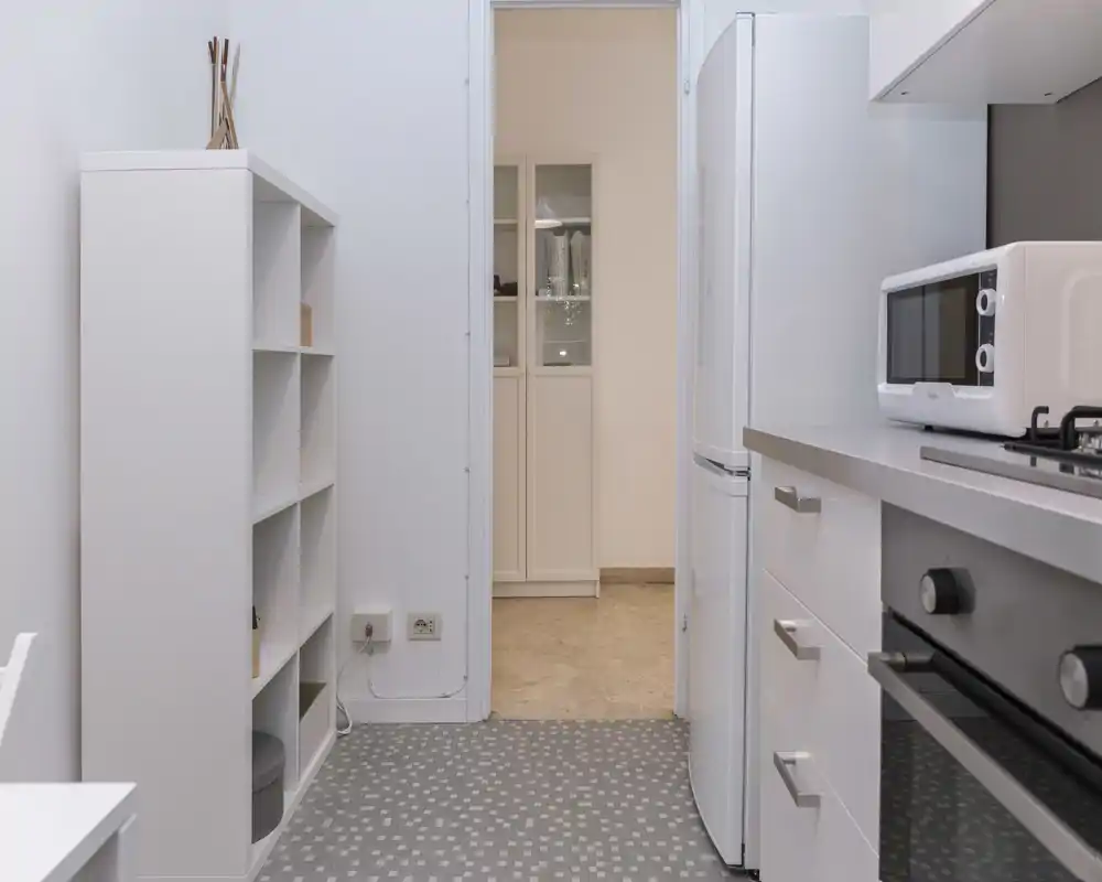 Cucina compatta e moderna con mobili bianchi, frigorifero, forno e microonde, luminosa e ordinata, perfetta per annunci di affitto.