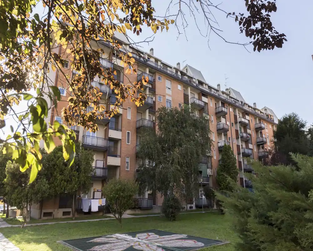 Vista esterna di un condominio residenziale con balconi, piccolo prato e alberi maturi illuminati da una luce calda — ideale per mostrare la facciata e gli spazi esterni comuni.