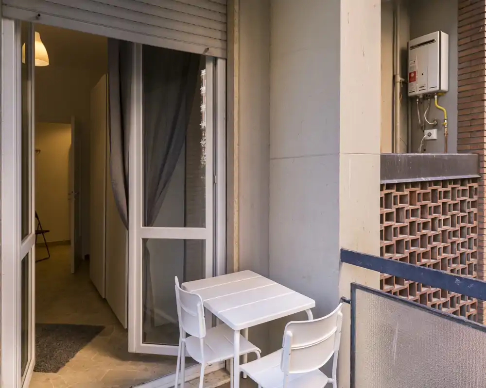 Piccolo balcone arredato con un tavolino bianco e due sedie che si aprono dall'appartamento; ideale per un caffè mattutino o un angolo esterno compatto.