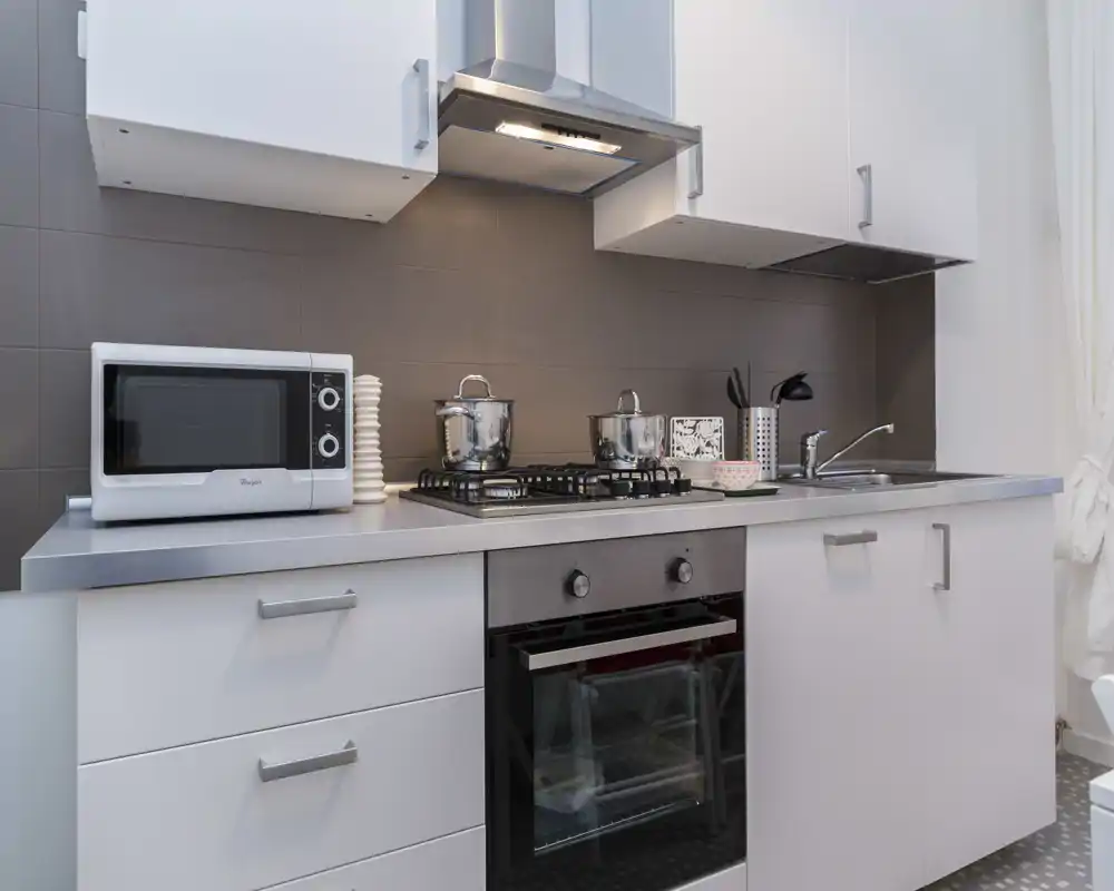 Cucina moderna e compatta con piano in acciaio, piano cottura a gas e forno incassato. Piccoli elettrodomestici e utensili sono ordinati, creando un ambiente funzionale e curato.