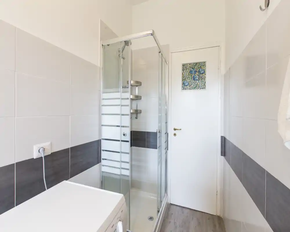 Baño moderno y luminoso con ducha acristalada, azulejos en paredes y distribución compacta. Espacio limpio y bien iluminado, ideal para alquileres de corta estancia.