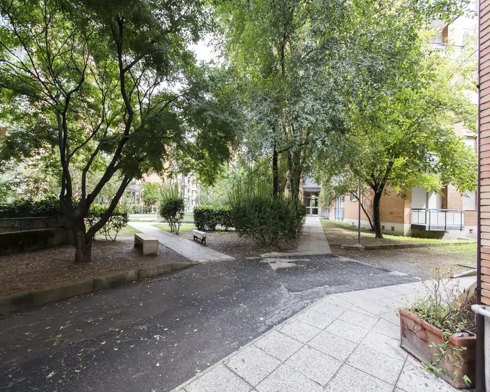 Tranquilo patio comunitario con árboles maduros, senderos pavimentados y bancos — un espacio verde compartido ideal para relajarse fuera del edificio.