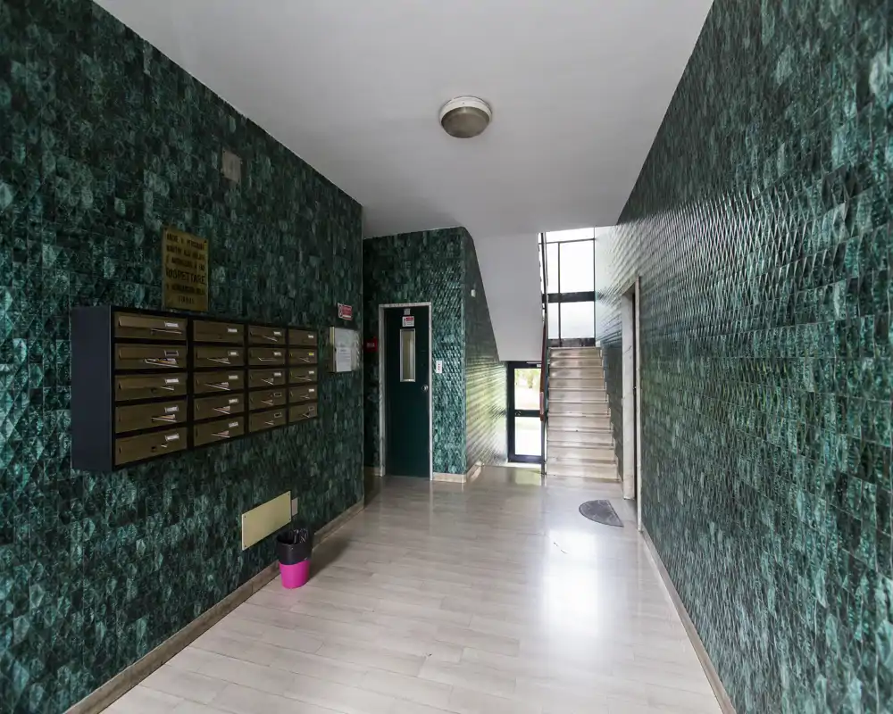 Entrada del edificio bien iluminada con paredes decoradas, buzones, escaleras y puerta del ascensor: zona de acceso práctica y ordenada.