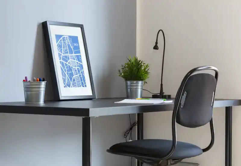 Coin bureau compact et moderne avec un bureau noir simple et une chaise, une affiche encadrée décorative et une petite plante en pot, formant un espace de travail soigné et fonctionnel.