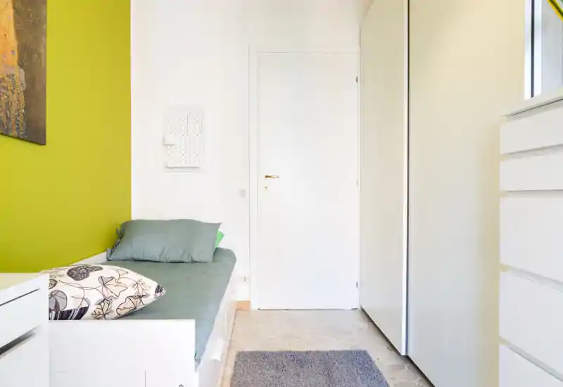 Dormitorio compacto y luminoso con cama individual junto a una pared verde, ropa de cama suave y almacenamiento práctico — ideal para una estancia acogedora.