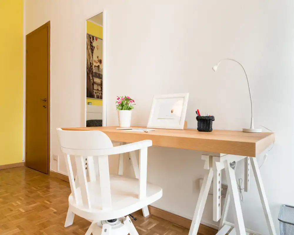 Espacio de trabajo limpio y luminoso con escritorio de madera, silla blanca giratoria, lámpara de escritorio y pequeña planta — ideal para teletrabajo o estudio.