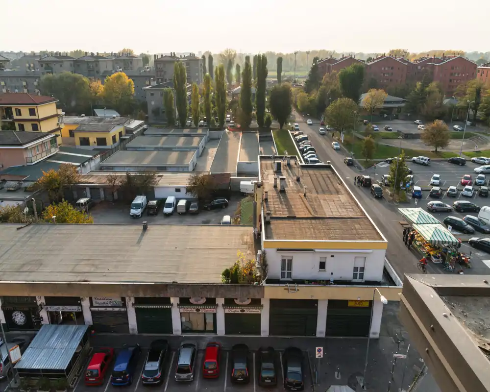Vista exterior urbana: tejados, coches aparcados y un puesto de mercado en la cálida luz de la tarde — adecuada para mostrar el exterior del edificio y la calle cercana.