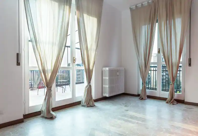 Espace de séjour lumineux et vide avec de grandes baies vitrées et voilages, donnant sur un balcon — idéal pour des photos d’annonce mettant en valeur la lumière naturelle et l’accès extérieur.