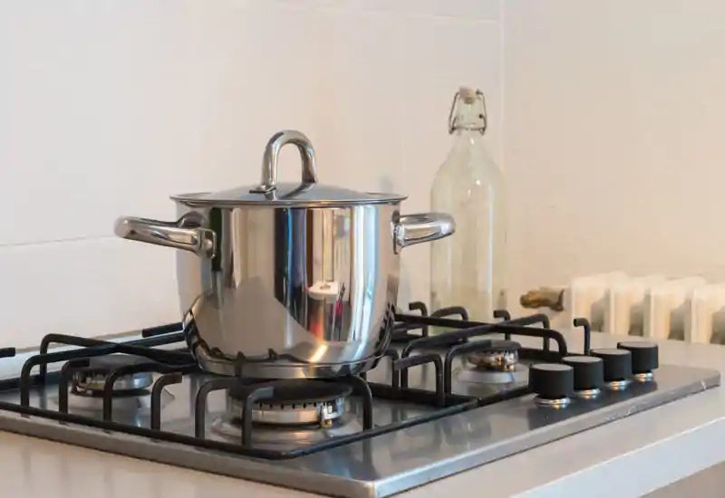Gros plan sur une cuisinière à gaz avec une casserole en inox ; détail de cuisine propre et bien éclairé, idéal pour une annonce locative.