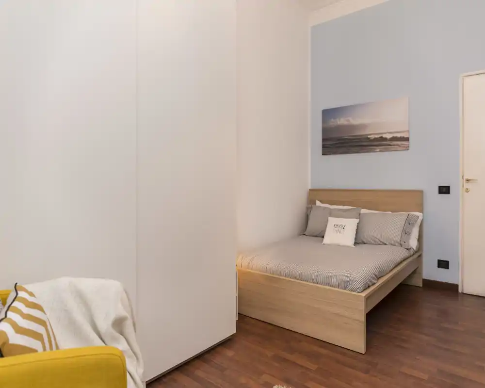 Tidy bedroom with a wooden double bed, soft linens and warm lighting; neutral walls and a coastal print add calm, modern character.