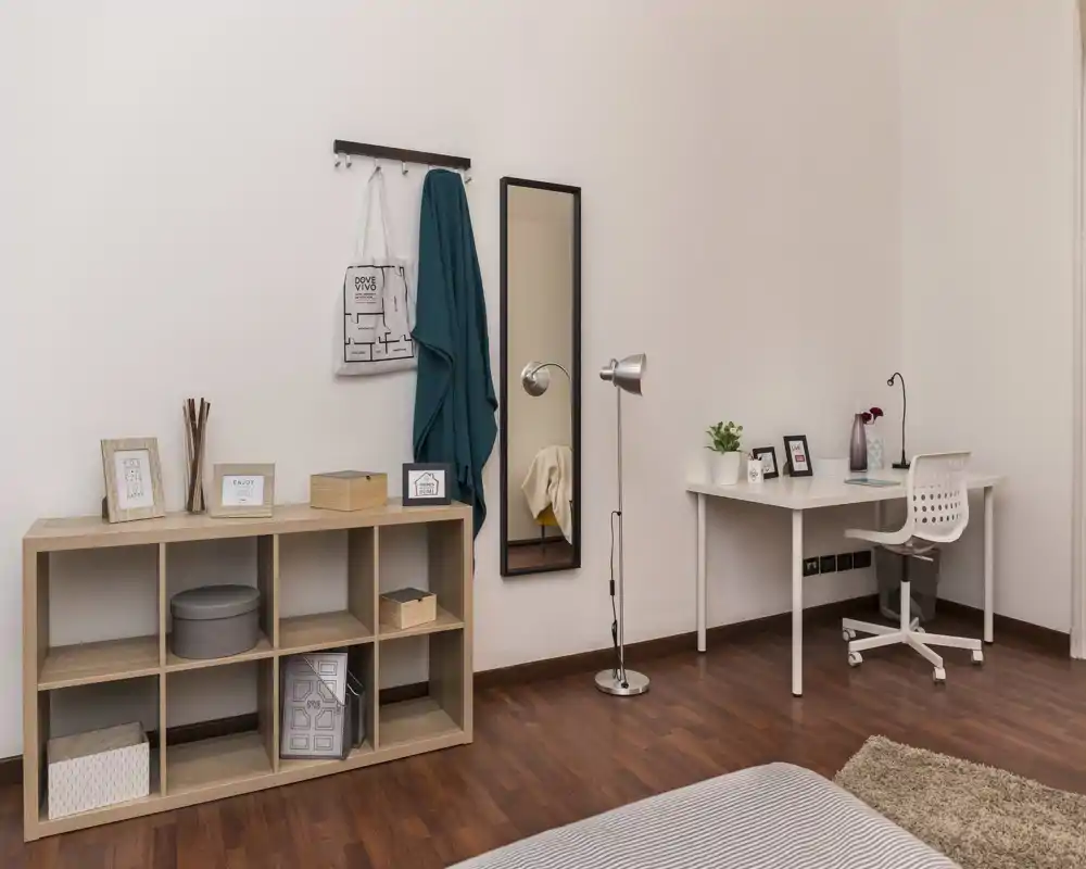 Bright, minimalist bedroom corner with a visible mattress edge, wooden shelving and a neat desk — a pleasant, functional sleeping and working area.