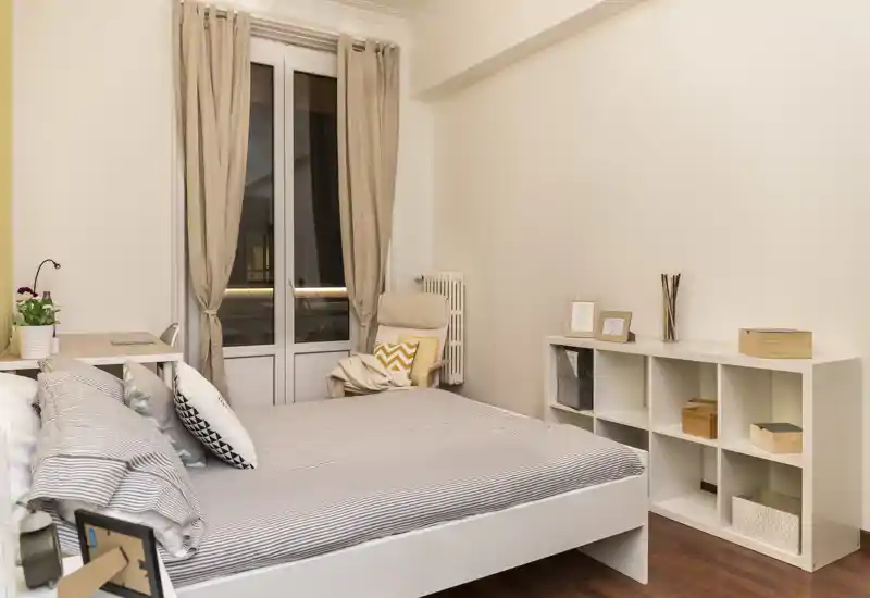 Dormitorio luminoso y ordenado con cama grande, escritorio, sillón cómodo y estantería — tonos neutros y textiles suaves que crean un ambiente tranquilo y acogedor.