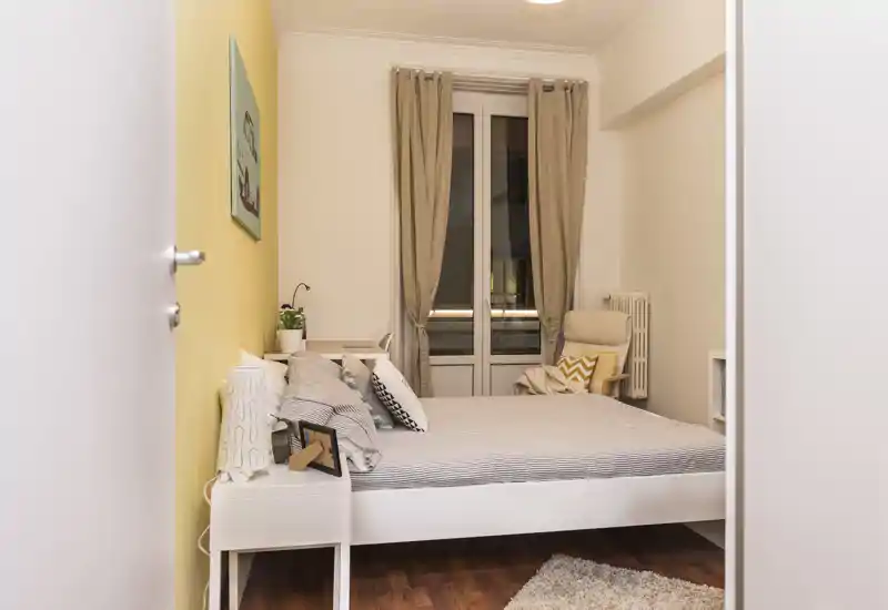 Bright, neatly staged bedroom with a double bed, soft textiles, and a cozy reading chair by the window — ideal for rental photos.