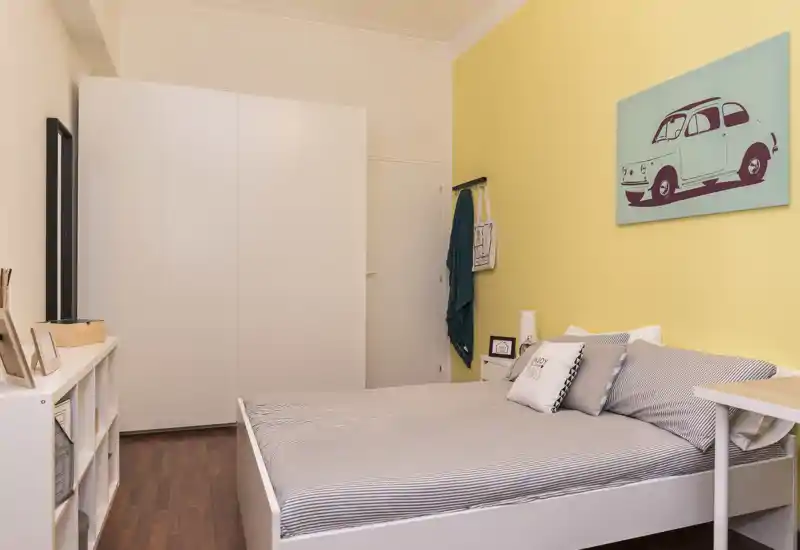 Dormitorio luminoso y bien presentado con cama doble, ropa de cama a rayas, armario y pared amarilla con cuadro — ideal para anuncios.