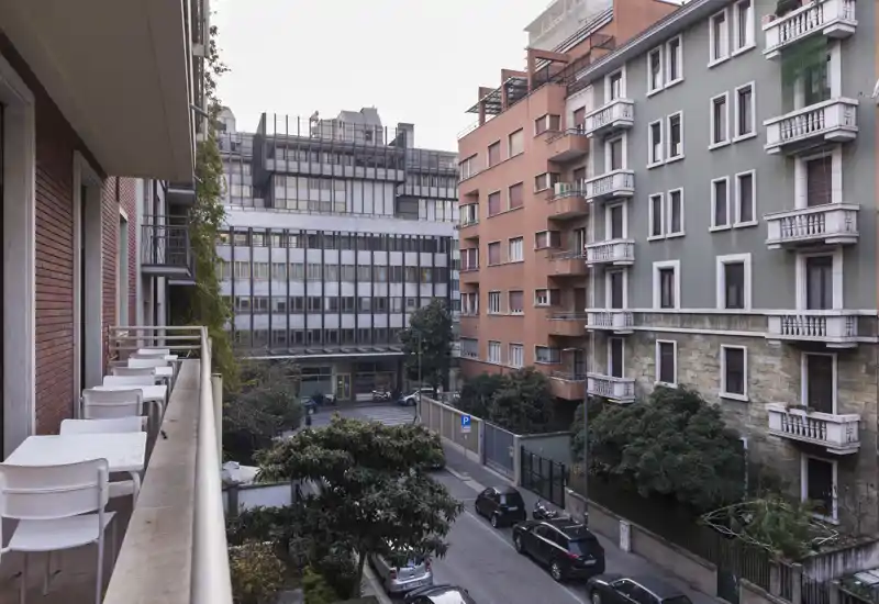 Quiet urban balcony overlooking a residential street with parked cars and neighboring apartment buildings — ideal for morning coffee with a city view.