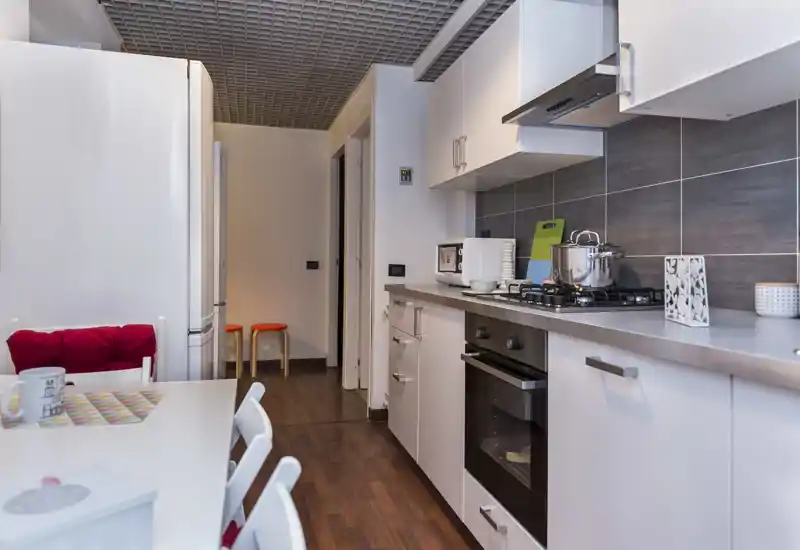 Cocina moderna equipada con muebles blancos, placa de gas y horno empotrado; suelo de madera cálido y mesa informal que la hacen acogedora y práctica para alquileres.