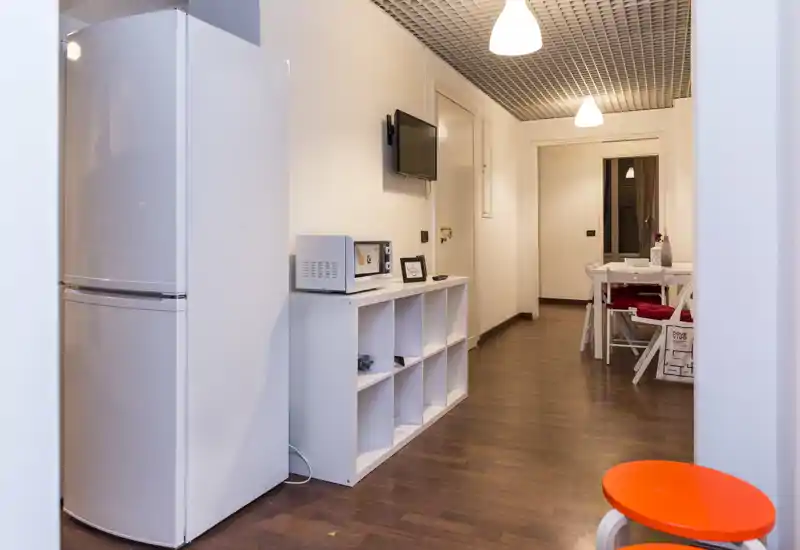 Compact kitchen area opening onto a small dining nook with a white table and chairs, wooden floors and warm overhead lighting—functional and tidy for short stays.