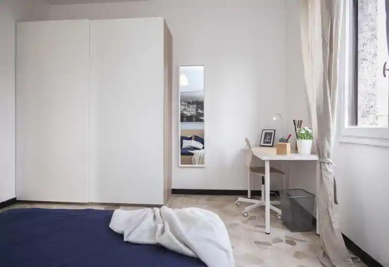 Bright, minimal bedroom with a large wardrobe, bedside mirror and a small desk by the window. Natural light and soft textiles create a calm, welcoming atmosphere ideal for short-term rentals.