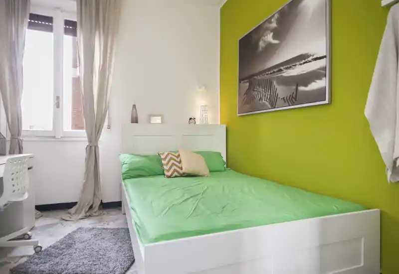 Dormitorio individual luminoso y bien decorado con cama blanca, ropa de cama verde y un cuadro en la pared. La luz natural y los textiles suaves lo hacen acogedor para estancias cortas.