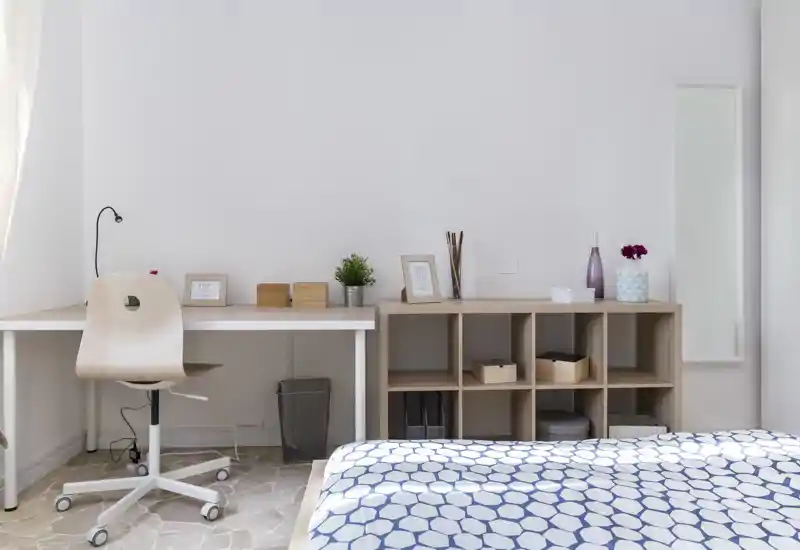 Bright, minimal bedroom with a patterned duvet, a work desk and wooden cubed shelving — a clean, airy space good for both rest and light work.
