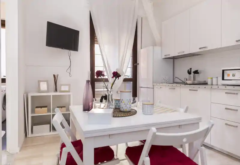Bright, modern kitchenette with a small dining table set for two. White cabinets, fridge and tasteful table décor create a welcoming space ideal for compact city stays.