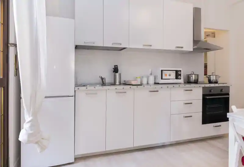Compact modern kitchen with white cabinets, integrated oven, microwave and refrigerator. Bright, clean and neatly arranged counter space ideal for a small apartment.