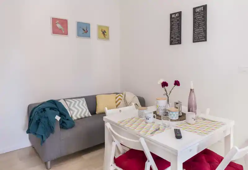 Bright, cozy living/dining corner with a small sofa, a white dining table and colorful cushions and décor — ideal for a compact apartment.