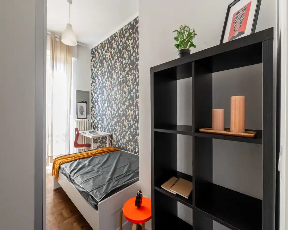 Dormitorio luminoso y con estilo, con pared de acento estampada, cama individual bien arreglada y un pequeño escritorio junto a la ventana — ideal para un alquiler acogedor y funcional.