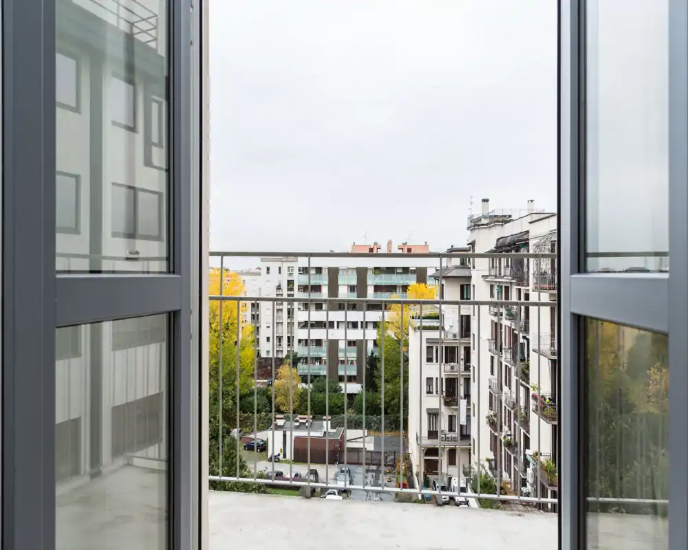 Balcón abierto enmarcado por puertas correderas, con vistas a edificios y copas de árboles — ideal para mostrar un pequeño espacio exterior urbano.