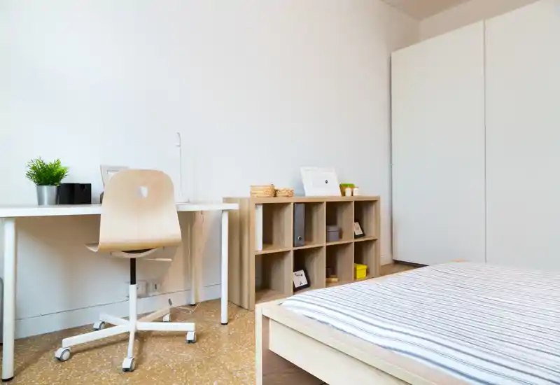 Camera da letto minimal e luminosa con struttura del letto in legno e biancheria a righe, una scrivania e scaffalatura: arredo pulito in stile nordico, ideale per una persona sola.