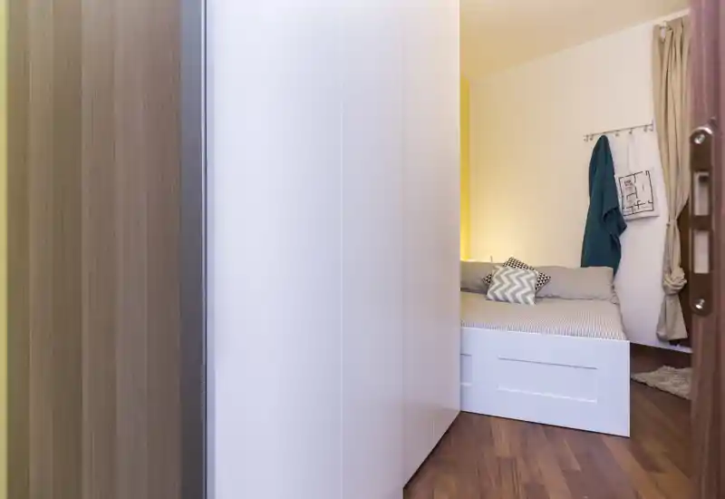 Compact bedroom with a white platform bed, decorative cushions and warm ambient lighting; tidy layout ideal for rental photos.