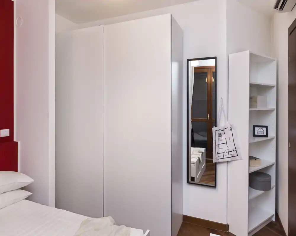 Angolo camera luminoso e ordinato con letto visibile, grande armadio bianco, specchio a figura intera e scaffalatura — stile moderno e minimal, ottimo per annunci.