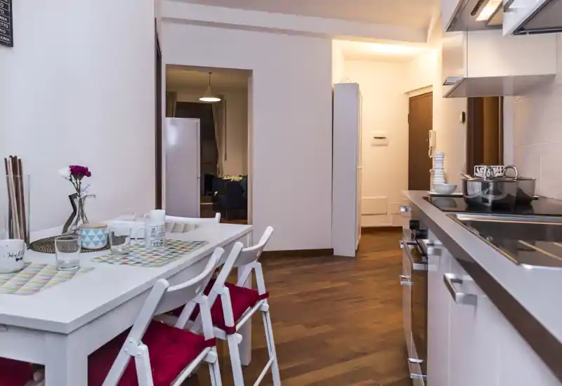 Cuisine ouverte avec table à manger pour quatre personnes ; rangements modernes, plaque à induction et parquet chaud créent un espace convivial et fonctionnel.